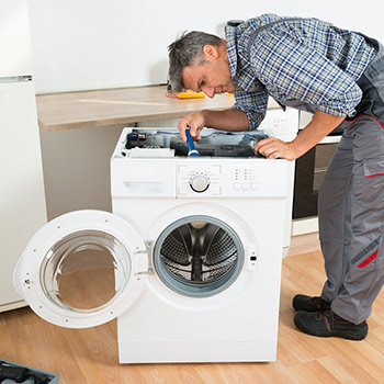 Fachmann leuchtet mit Taschenlampe in Waschmaschine